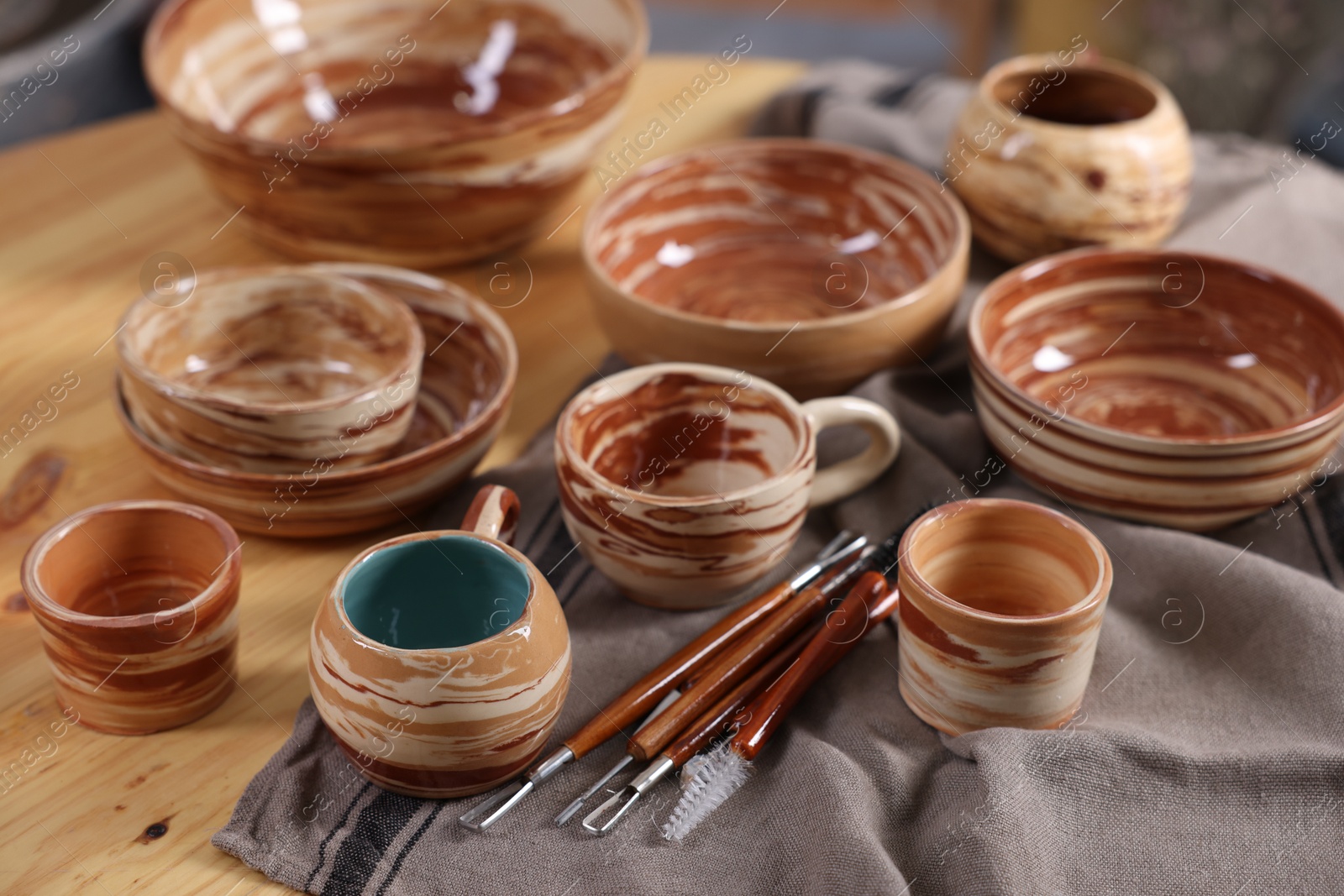 Photo of Different beautiful pottery and set of clay crafting tools on wooden table, closeup