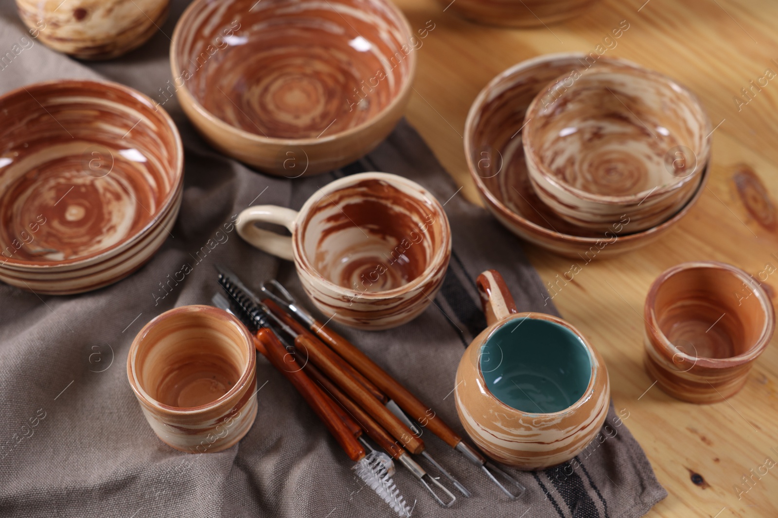 Photo of Different beautiful pottery and set of clay crafting tools on wooden table