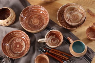 Photo of Different beautiful pottery and set of clay crafting tools on wooden table, flat lay