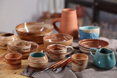 Photo of Different beautiful pottery and set of clay crafting tools on wooden table indoors, closeup