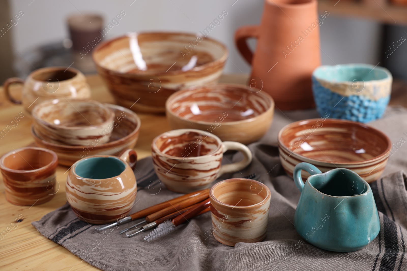 Photo of Different beautiful pottery and set of clay crafting tools on wooden table indoors, closeup