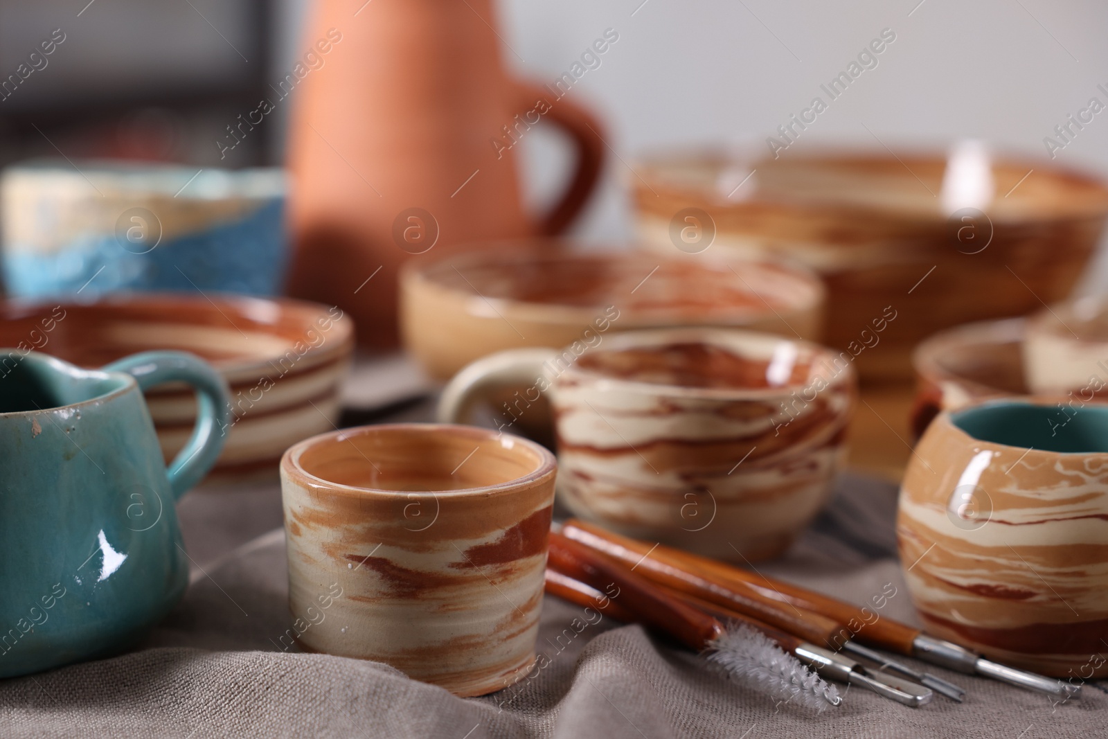 Photo of Different beautiful pottery and set of clay crafting tools on table indoors, closeup