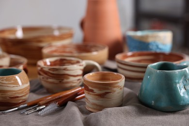 Photo of Different beautiful pottery and set of clay crafting tools on table indoors, closeup