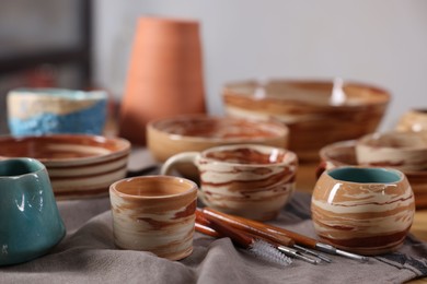 Photo of Different beautiful pottery and set of clay crafting tools on table indoors, closeup