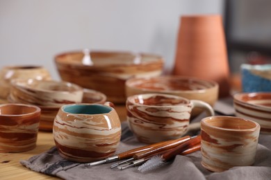 Photo of Different beautiful pottery and set of clay crafting tools on wooden table indoors, closeup