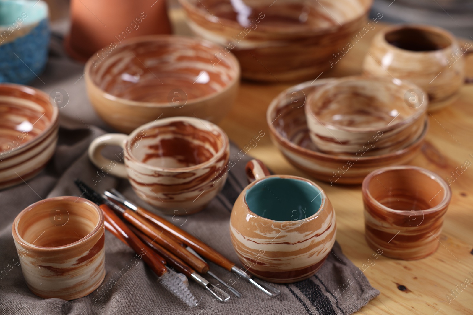 Photo of Different beautiful pottery and set of clay crafting tools on wooden table, closeup