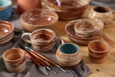 Photo of Different beautiful pottery and set of clay crafting tools on wooden table, closeup