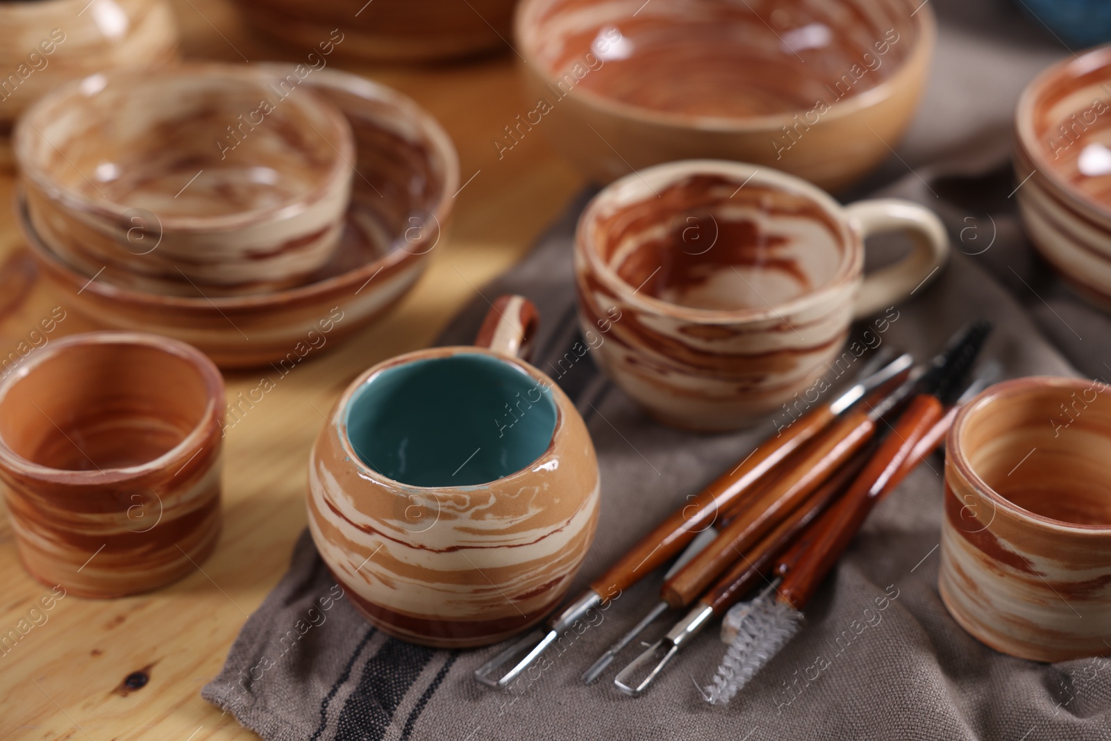 Photo of Different beautiful pottery and set of clay crafting tools on wooden table, closeup