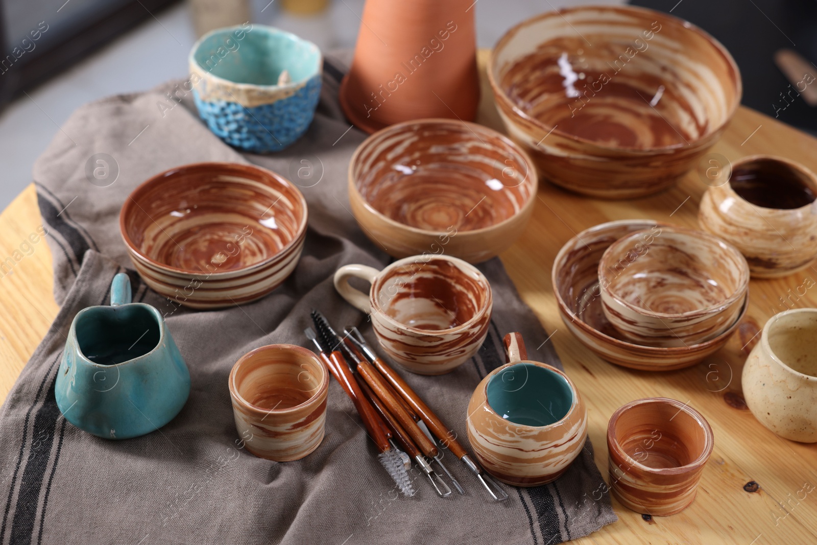 Photo of Different beautiful pottery and set of clay crafting tools on table indoors