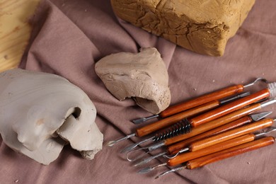 Photo of Set of different crafting tools and pieces of clay on wooden table, top view