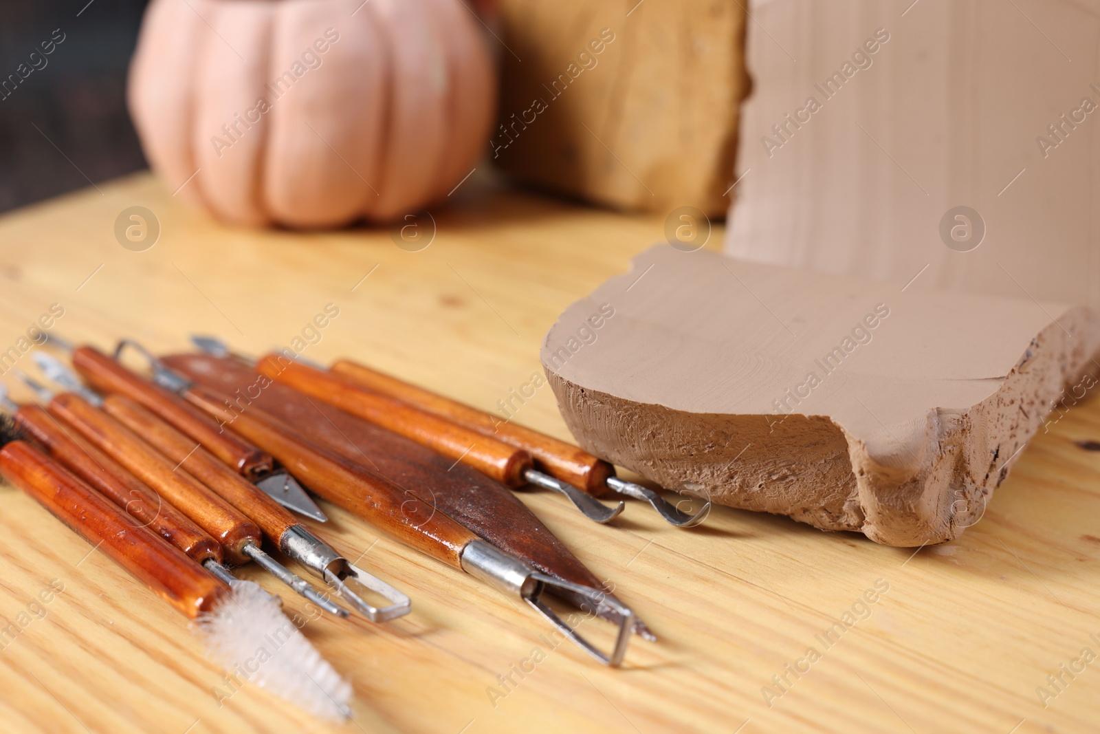 Photo of Set of different crafting tools and pieces of clay on wooden table, closeup