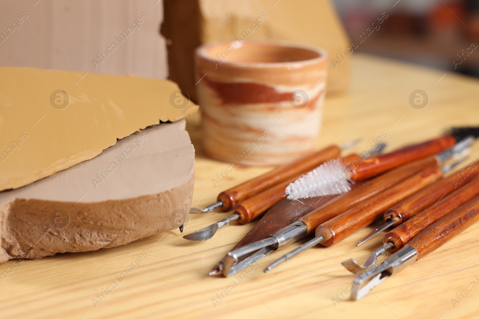 Photo of Set of different crafting tools and pieces of clay on wooden table, closeup