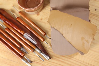 Photo of Set of different crafting tools and pieces of clay on wooden table, flat lay