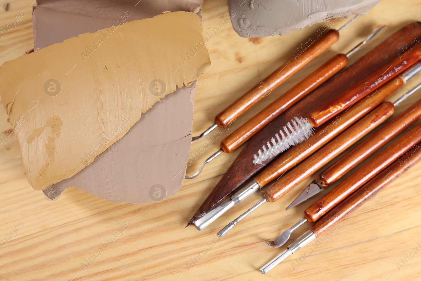 Photo of Set of different crafting tools and pieces of clay on wooden table, flat lay