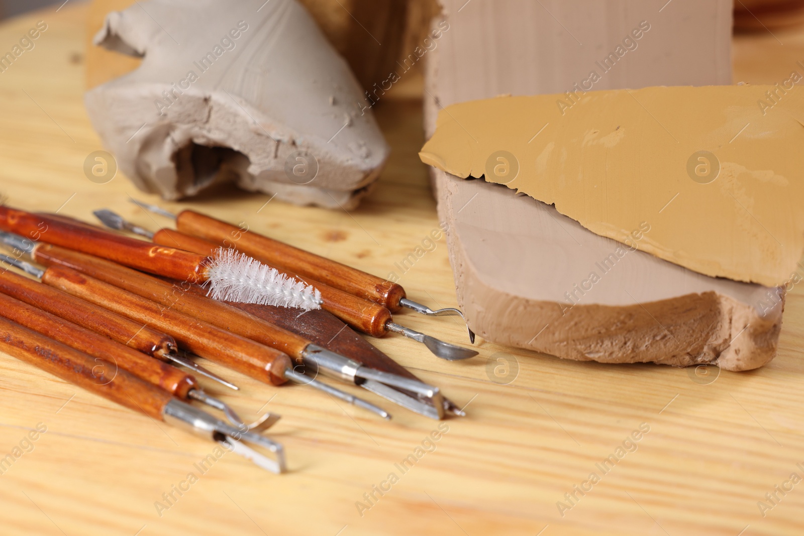 Photo of Set of different crafting tools and pieces of clay on wooden table, closeup