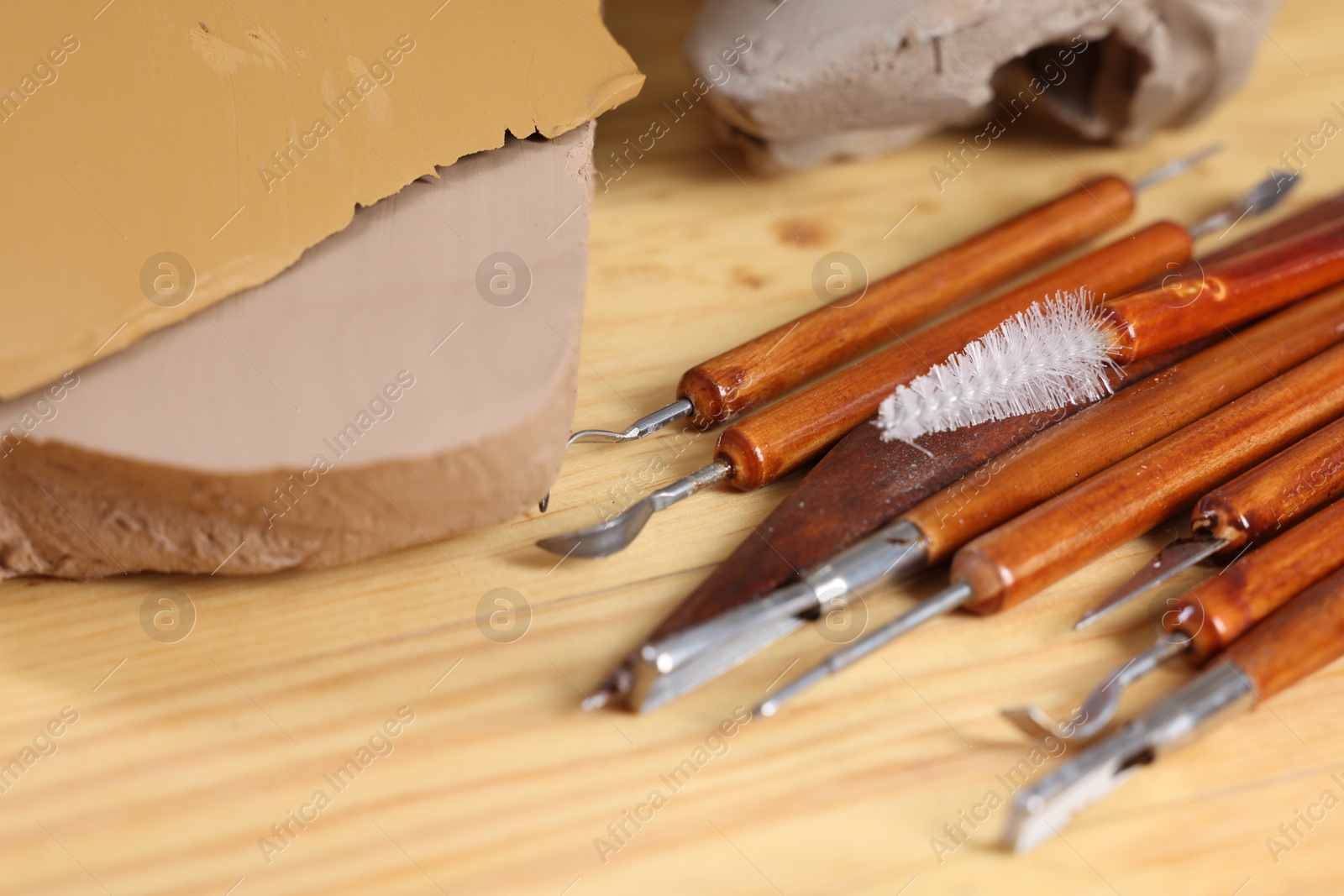 Photo of Set of different crafting tools and pieces of clay on wooden table, closeup