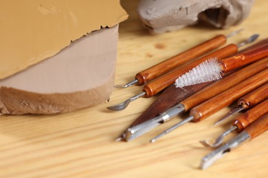 Photo of Set of different crafting tools and pieces of clay on wooden table, closeup