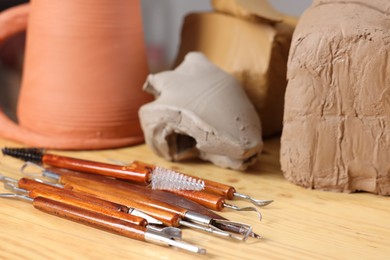 Photo of Set of different crafting tools and pieces of clay on wooden table, closeup