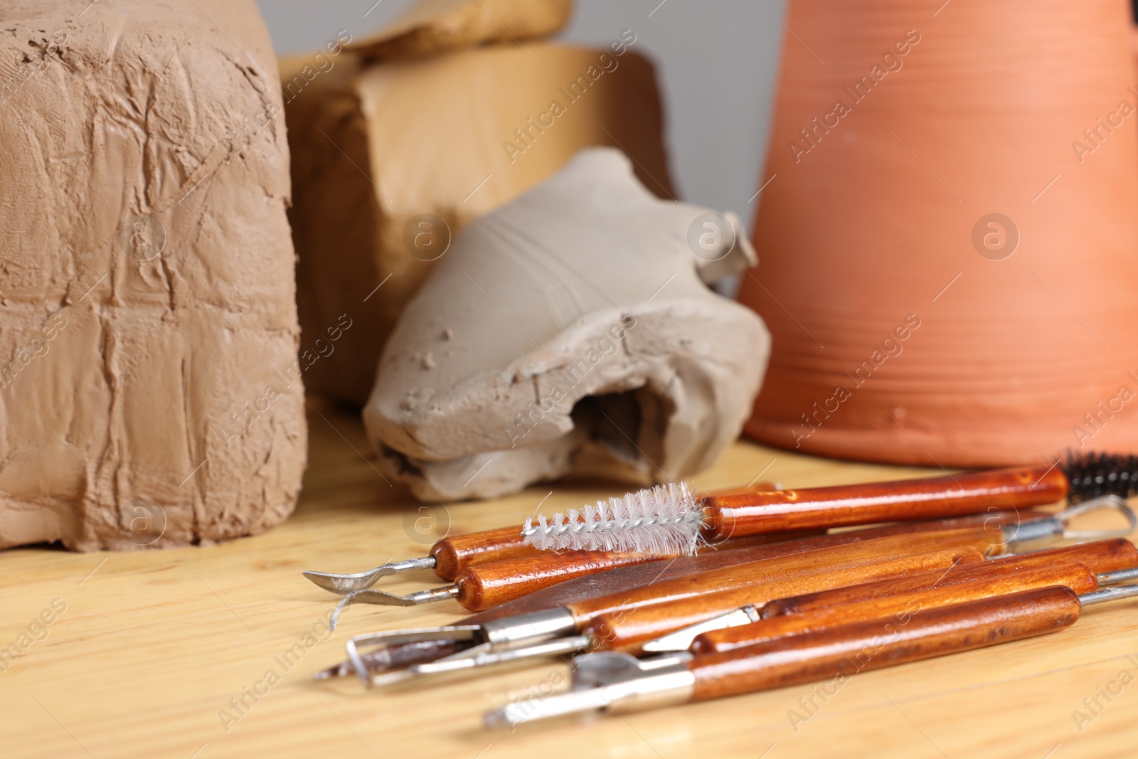 Photo of Set of different crafting tools and pieces of clay on wooden table, closeup