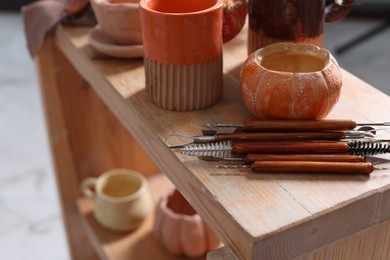 Photo of Set of different crafting tools and pottery on wooden shelf indoors, closeup