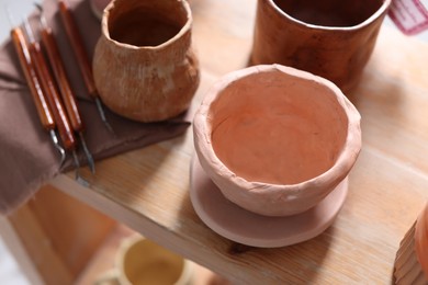 Photo of Beautiful pottery and set of different crafting tools on wooden shelf indoors, closeup