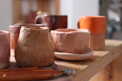 Photo of Set of different crafting tools and pottery on wooden shelf indoors, closeup