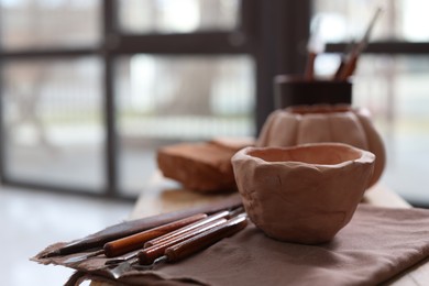 Photo of Handmade ceramic bowl and set of different crafting tools on shelf indoors, closeup. Space for text