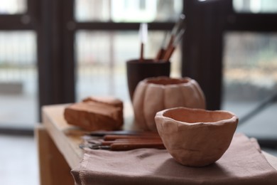 Photo of Handmade ceramic bowl and set of different crafting tools on shelf indoors