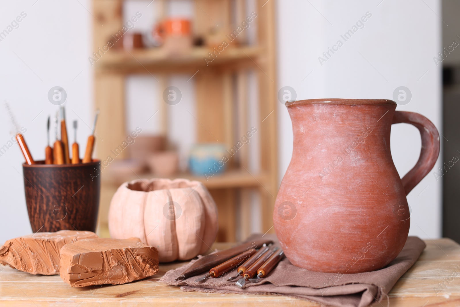 Photo of Beautiful pottery, crafting tools and pieces of clay on wooden table in workshop