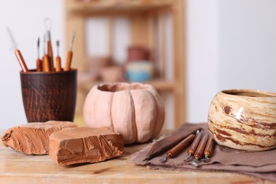 Photo of Beautiful pottery, crafting tools and pieces of clay on wooden table in workshop