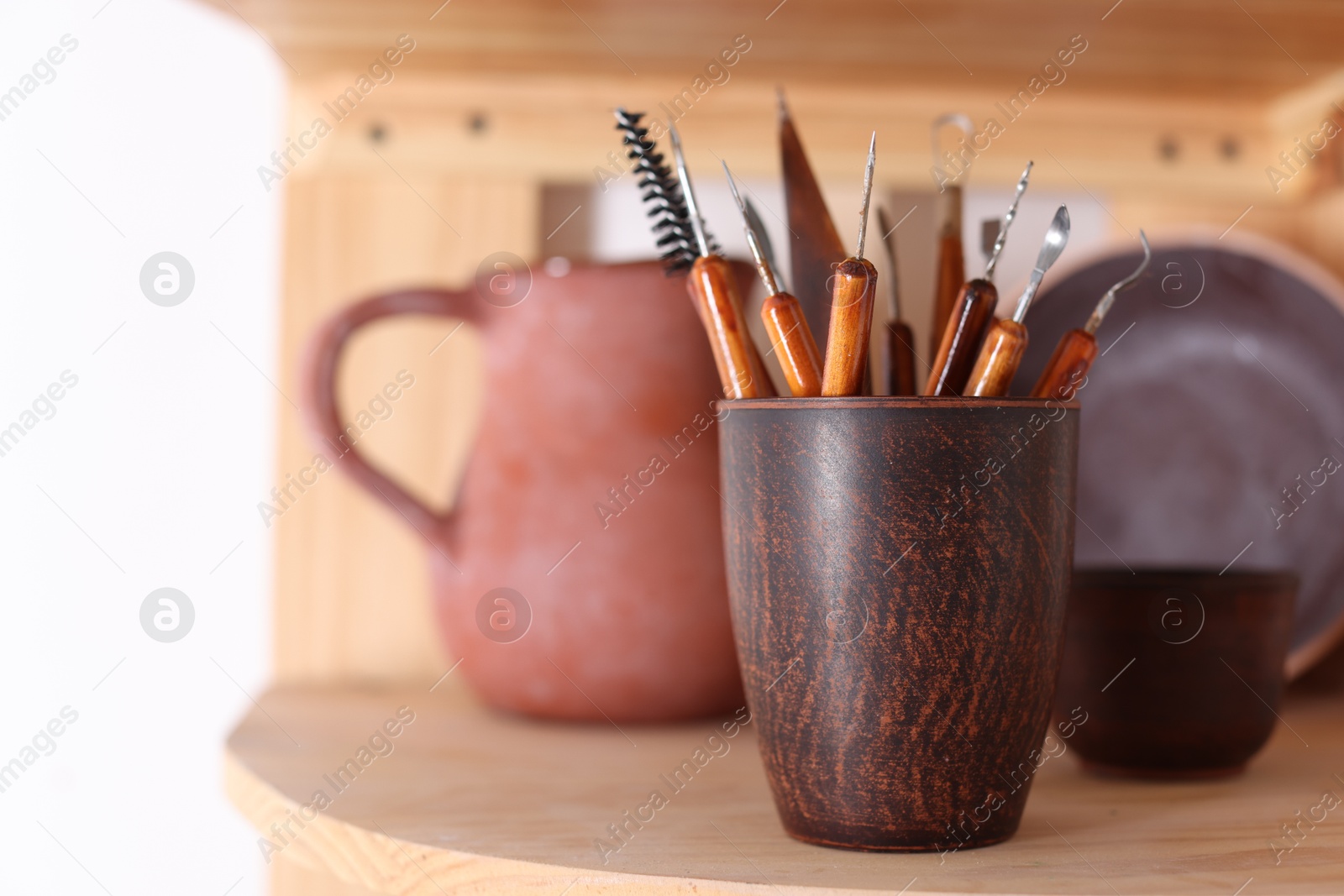 Photo of Set of different crafting tools and ceramic holder on wooden shelf indoors, closeup. Space for text