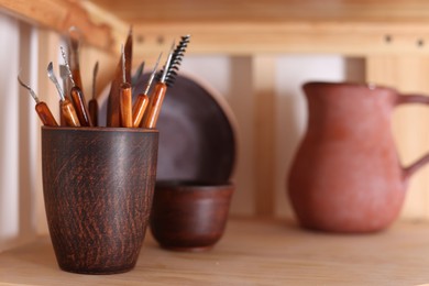 Photo of Set of different crafting tools and ceramic holder on wooden shelf indoors, closeup. Space for text