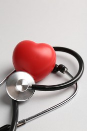 Photo of Cardiology. Stethoscope and red decorative heart on light gray background, closeup. Space for text