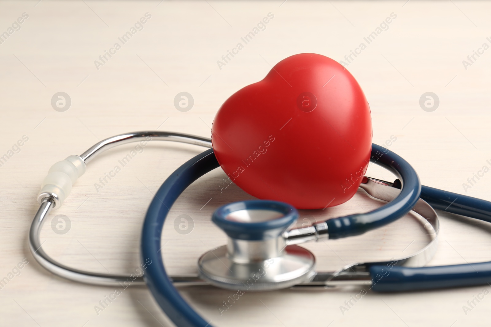 Photo of Cardiology. Stethoscope and red decorative heart on light wooden table, closeup