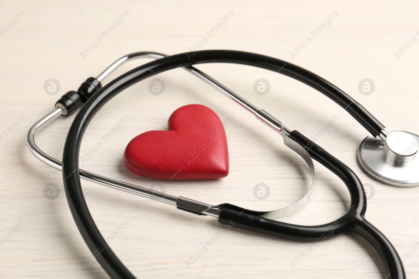 Photo of Cardiology. Stethoscope and red decorative heart on light wooden table, closeup