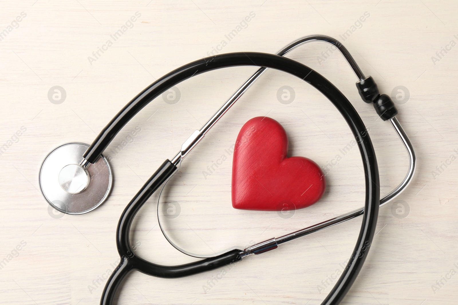 Photo of Cardiology. Stethoscope and red decorative heart on light wooden table, flat lay