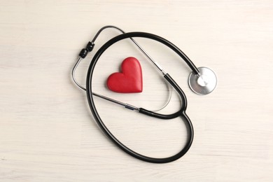 Photo of Cardiology. Stethoscope and red decorative heart on light wooden table, flat lay