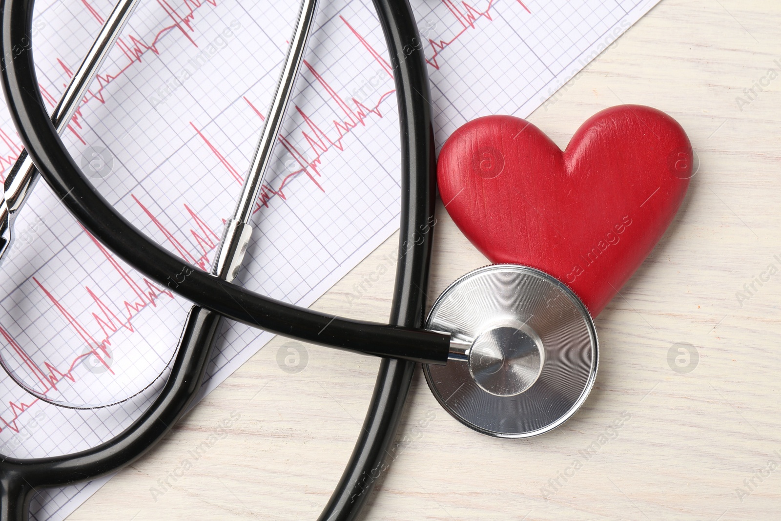 Photo of Cardiology. Stethoscope, cardiogram and red decorative heart on light wooden table, flat lay