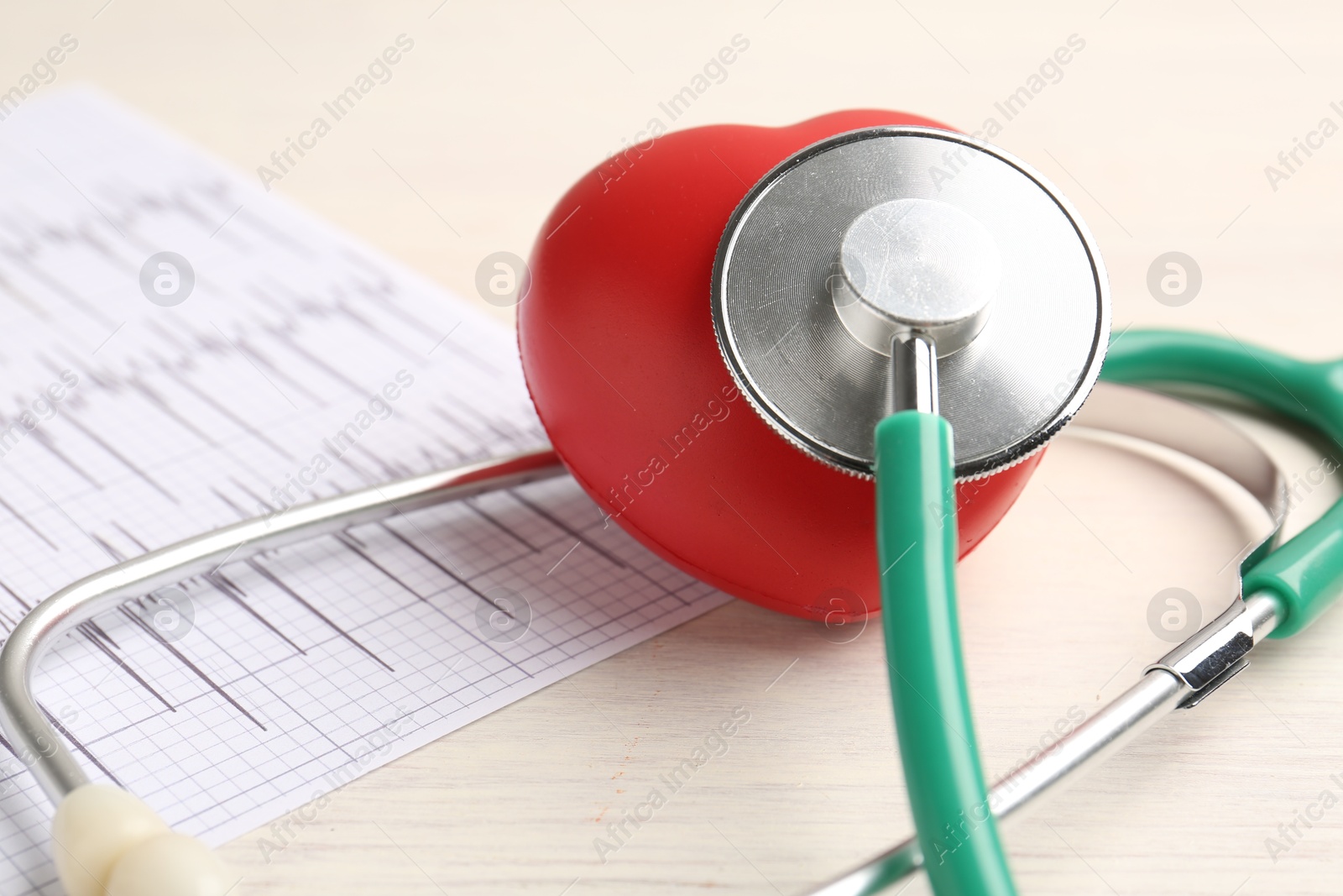 Photo of Cardiology. Stethoscope, cardiogram and red decorative heart on light wooden table, closeup