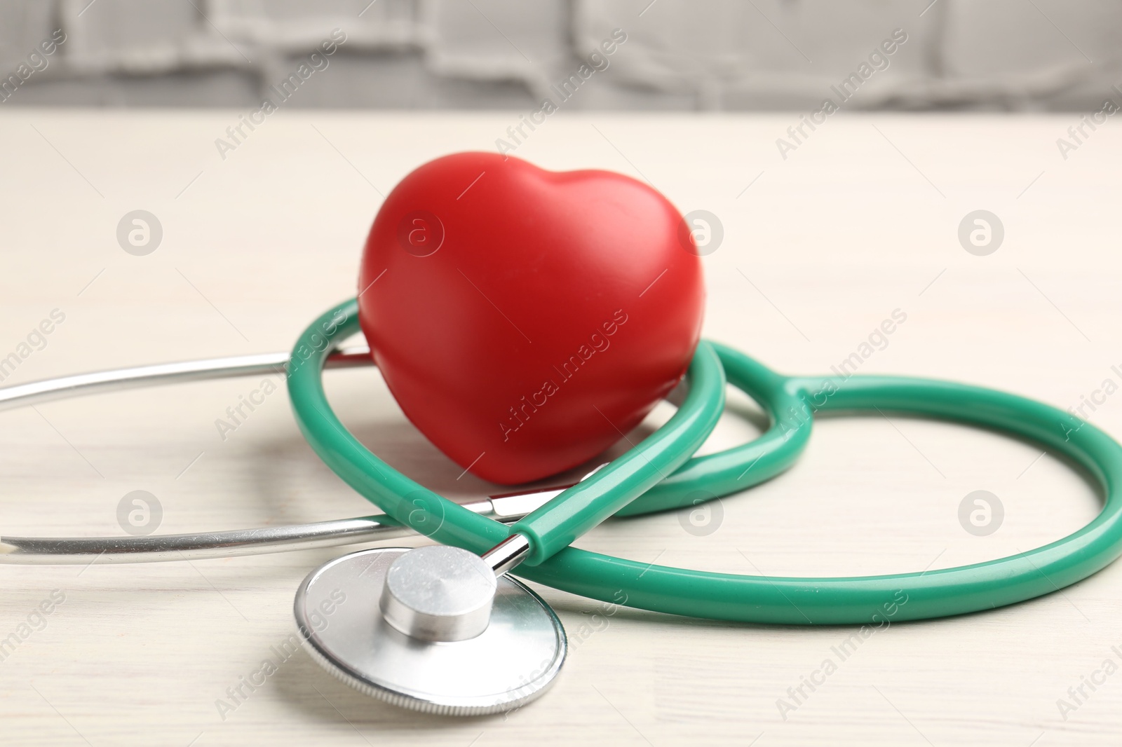 Photo of Cardiology. Stethoscope and red decorative heart on light wooden table, closeup