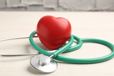 Photo of Cardiology. Stethoscope and red decorative heart on light wooden table, closeup