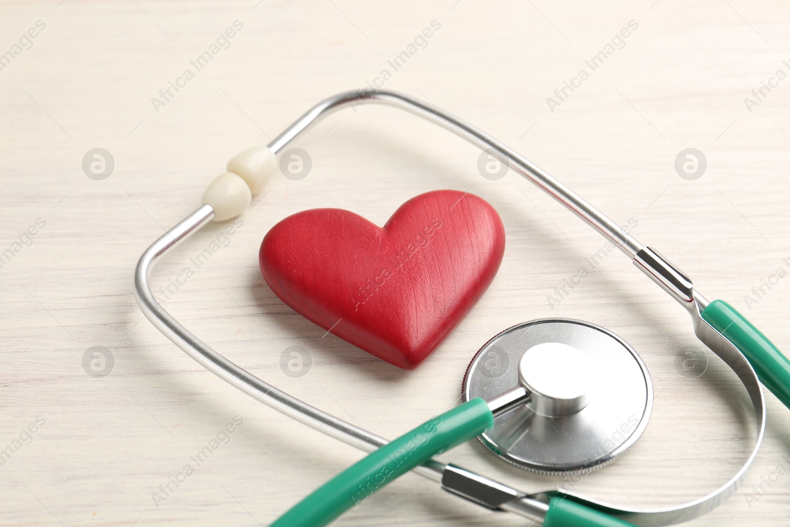 Photo of Cardiology. Stethoscope and red decorative heart on light wooden table, closeup