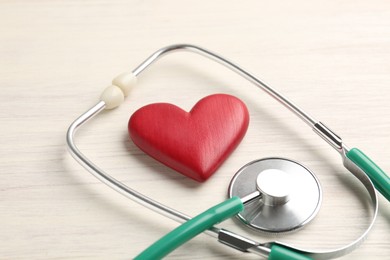 Photo of Cardiology. Stethoscope and red decorative heart on light wooden table, closeup