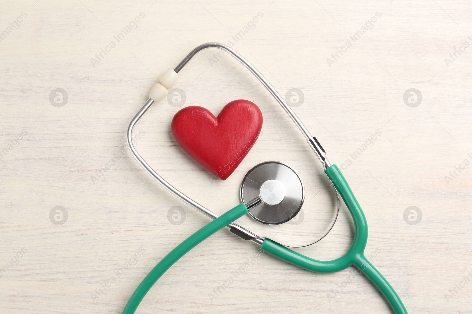 Photo of Cardiology. Stethoscope and red decorative heart on light wooden table, flat lay