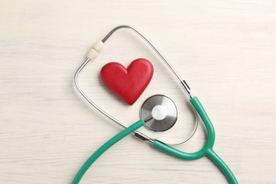 Photo of Cardiology. Stethoscope and red decorative heart on light wooden table, flat lay