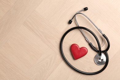 Photo of Cardiology. Stethoscope and red decorative heart on wooden table, flat lay. Space for text