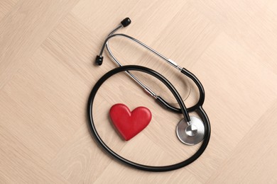 Photo of Cardiology. Stethoscope and red decorative heart on wooden table, flat lay