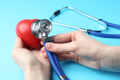 Photo of Cardiology. Woman with stethoscope and red decorative heart on light blue background, closeup