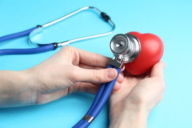 Photo of Cardiology. Woman with stethoscope and red decorative heart on light blue background, closeup