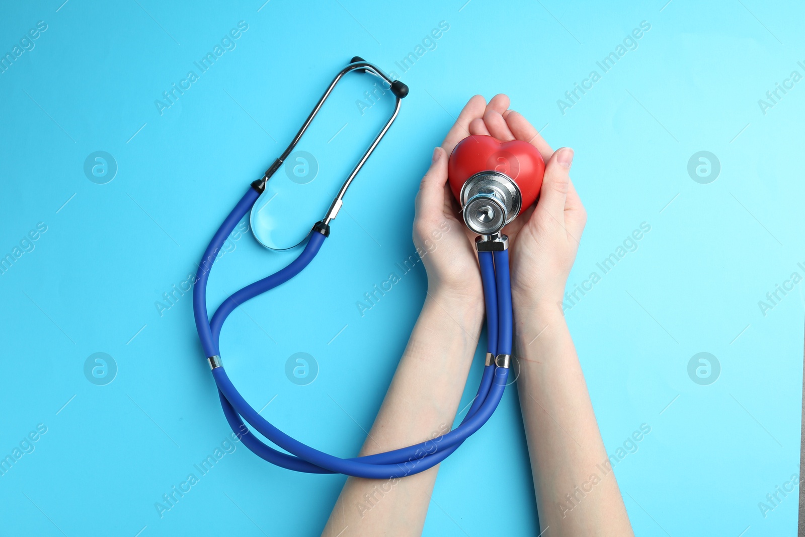 Photo of Cardiology. Woman with stethoscope and red decorative heart on light blue background, top view